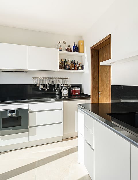Bright modern kitchen with white handleless cabinets, black granite worktops, and stainless steel Gaggenau appliances.