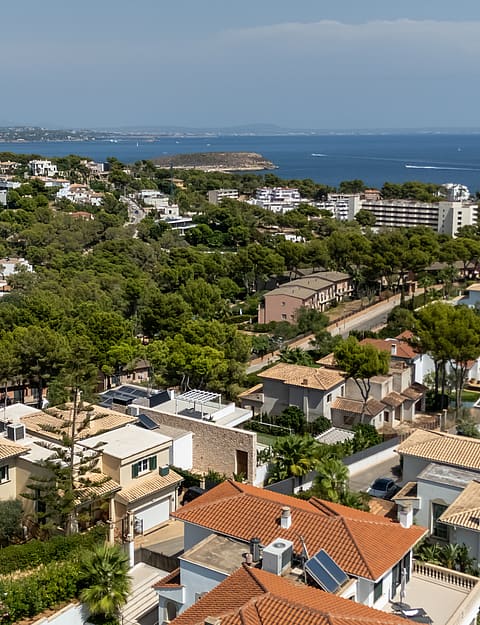 High-angle aerial photograph of the coastal residential neighborhood in Cala Vinyes, showing Mediterranean villas with terracotta roofs set among pine trees and sea views.