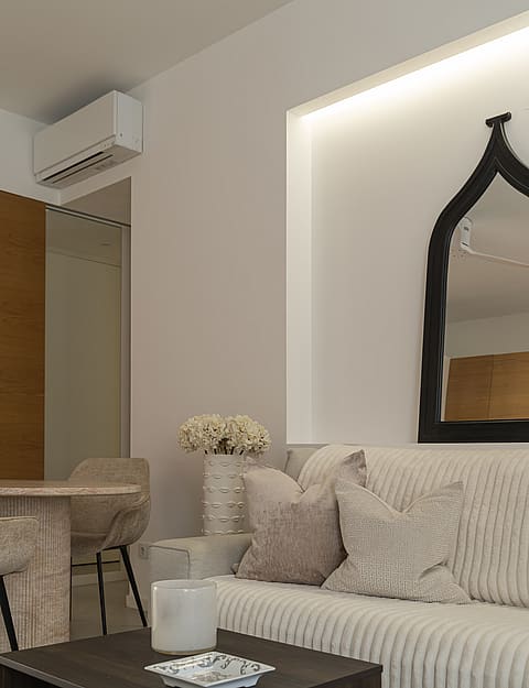 A modern living area featuring a ribbed beige sofa, dark wood coffee table, and an arched black-framed wall mirror.