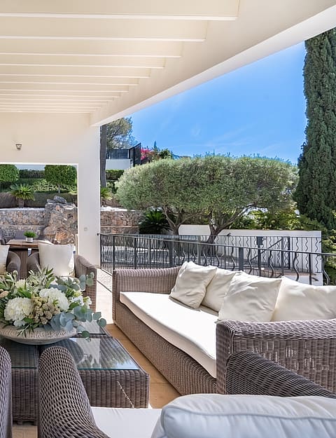 Covered outdoor terrace with rattan sofa set and far-reaching sea and mountain views at a villa in Son Vida, Mallorca