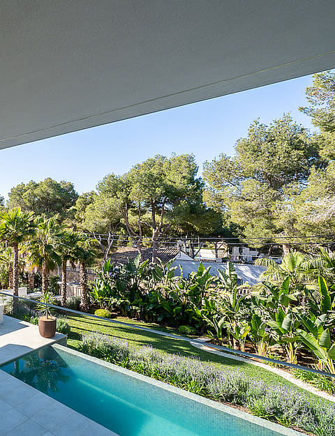 A wide, covered terrace with natural stone walls and a glass balustrade, overlooking a private garden with a swimming pool.