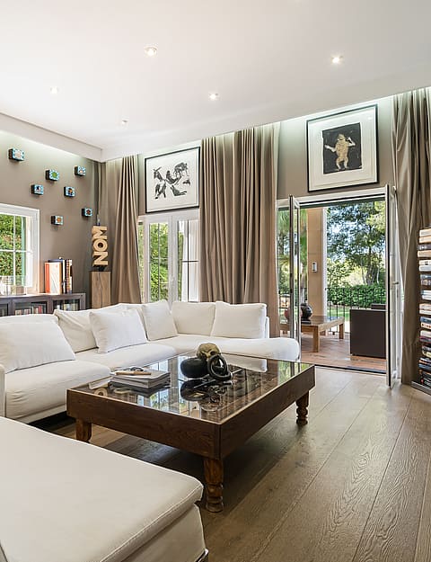 Spacious living room featuring white modular sofas, a central dark wood coffee table, and floor-to-ceiling curtains.