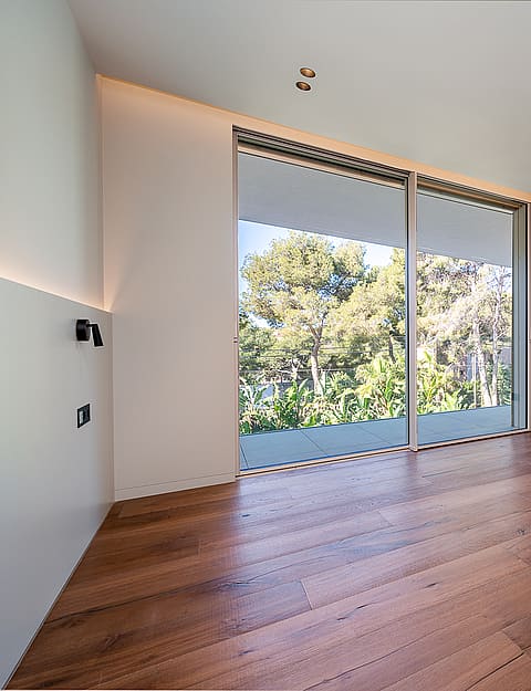 Empty bedroom with wide-plank oak flooring, white walls, recessed ceiling lights, and large sliding glass door to terrace.