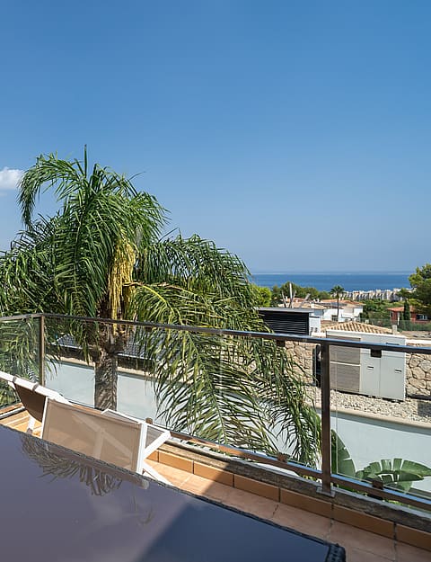 An elevated terrace with a dark outdoor table, glass railing, and distant views of the sea and green landscape.
