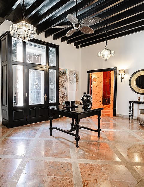 A spacious entrance hall in a townhouse featuring polished stone floors, dark wood beamed ceilings, and an ornate black frame partition.