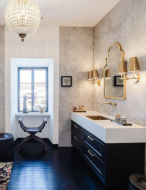 A modern bathroom featuring grey marble walls, a glass walk-in shower, a dark wood vanity with a stone basin, and gold accents.