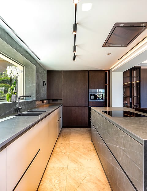 Modern open-plan kitchen featuring a large stone-topped island, dark wood cabinetry, and recessed ceiling track lighting.