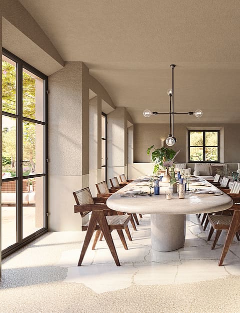 Dining room with a large oval stone table and wooden chairs, set against stone walls and large black-framed glass doors.