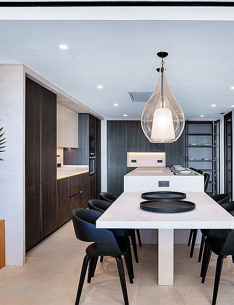 Modern open-plan kitchen with a large white island, dark cabinetry, and a light-colored natural stone feature wall.