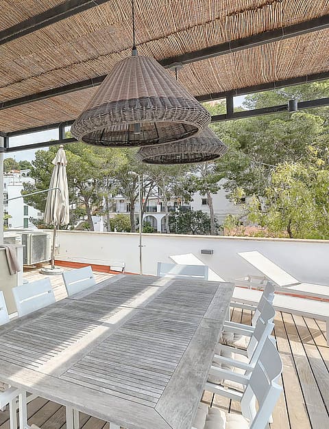 Covered outdoor terrace featuring a built-in kitchenette, dining table with seating, and wooden decking under a pergola.