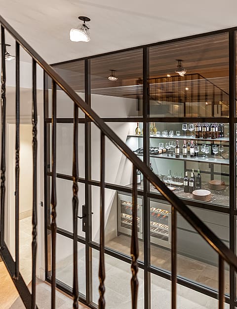 Wrought iron staircase railing in front of a climate-controlled glass wine cellar with internal shelving and lighting.