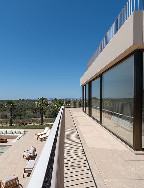 An elevated terrace with glass railings overlooking a swimming pool, sun loungers, and distant mountain landscape.