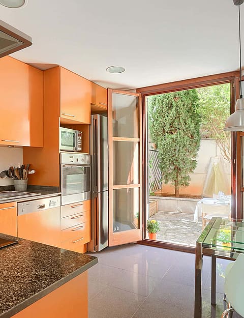 Modern kitchen with orange cabinetry, granite countertops, and glass door leading to a private outdoor garden area.