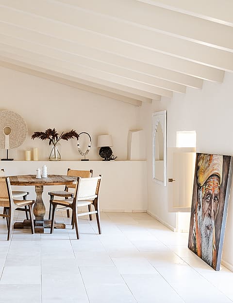 Dining room featuring a round wooden table, white stone floors, and a vaulted ceiling with exposed white-painted beams.