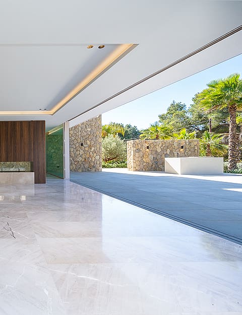 Modern open-plan kitchen with a stone island, floor-to-ceiling sliding glass doors, and polished marble flooring.