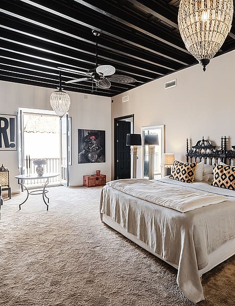 A spacious master bedroom in a Sencelles townhouse featuring a black exposed beam ceiling, a wrought iron bed, and neutral walls.