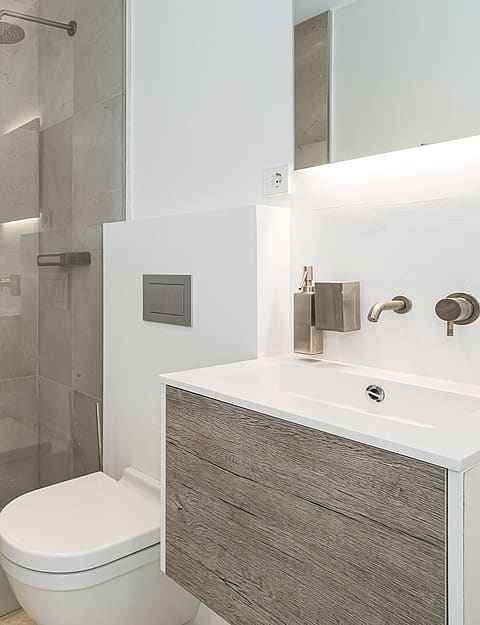 Modern bathroom featuring a wall-mounted floating vanity with wood-grain finish, white countertop, glass walk-in shower, and concealed toilet flush plate.
