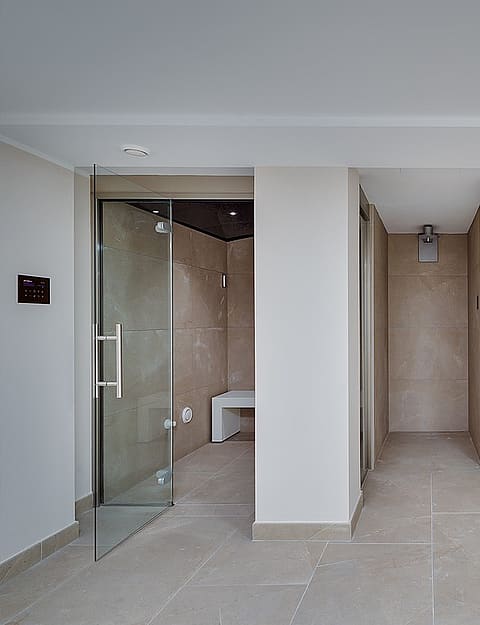 Glass-enclosed steam room with marble-effect tiles alongside a Finnish sauna with cedar benching and warm interior lighting