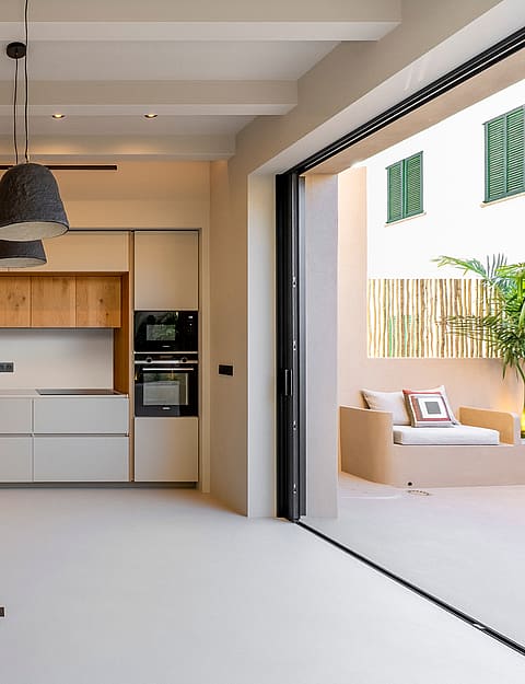 Modern kitchen with white and oak cabinetry, micro-cement floors, and sliding glass doors leading to a sun-drenched terrace.
