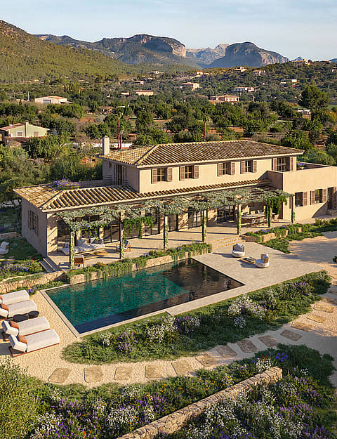 Aerial view of a traditional stone finca with a swimming pool, pergola-covered terrace, and surrounding Mediterranean gardens.