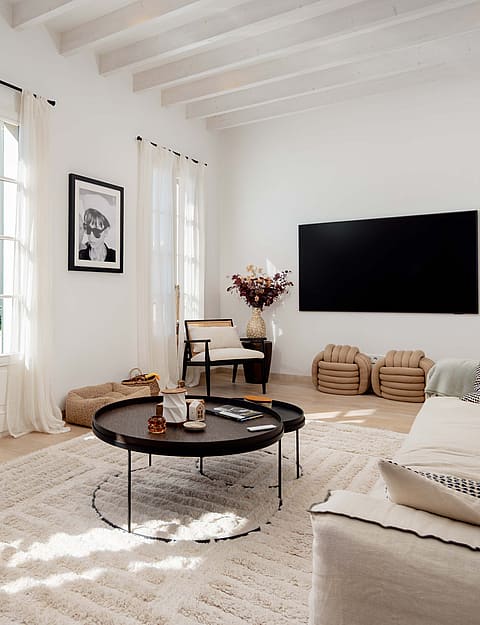 A bright living room in Santa Catalina with white walls, exposed white wooden ceiling beams, and French doors with linen curtains.