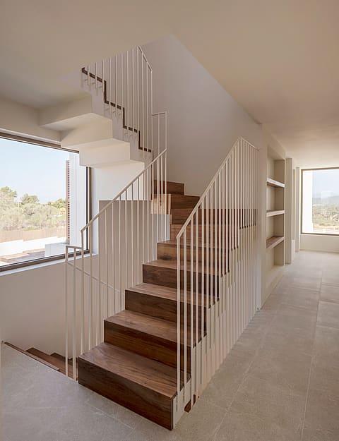 A staircase with dark wood treads and a white metal spindle railing, set against white walls with a large window.