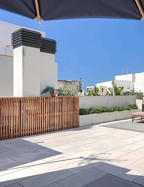 A rooftop terrace featuring a wooden outdoor kitchen, barbecue grill, and stone flooring under a clear blue sky.