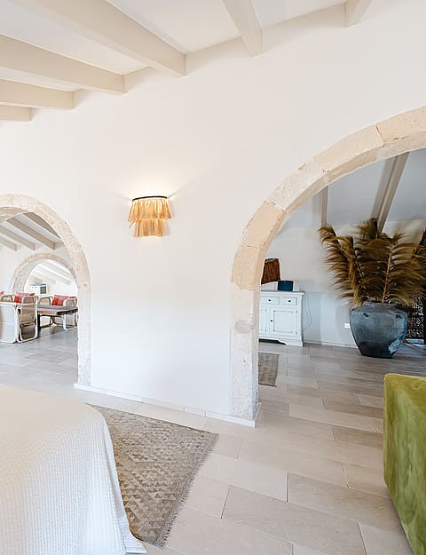 A spacious bedroom featuring white vaulted ceilings, limestone arches, and light stone flooring in a historic townhouse.