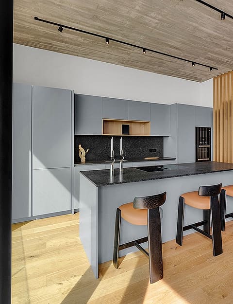 Modern open-plan kitchen featuring a gray island, oak wood slat room divider, light wood flooring, and track lighting.
