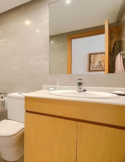 A bathroom featuring a light wood vanity, a wall-mounted mirror, a glass-enclosed bathtub, and neutral wall tiles.