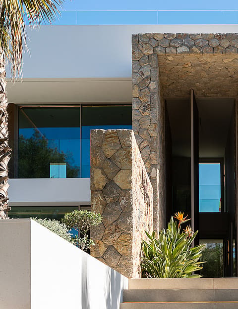 Front entrance of a modern villa featuring a central stone-clad column, white exterior walls, and a recessed doorway.