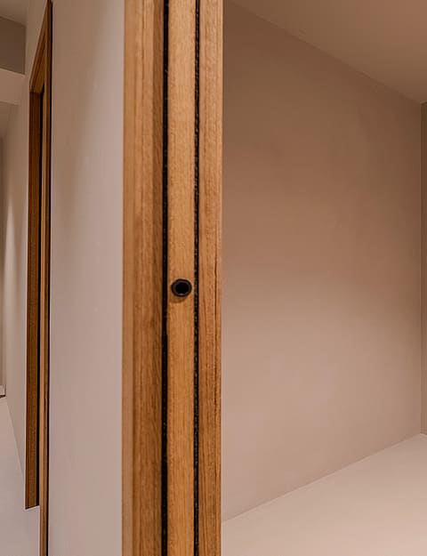 Interior view of a minimalist bathroom featuring neutral plaster walls, a central partition, and black horizontal blinds.