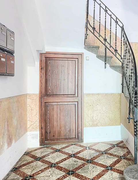 A staircase with terrazzo steps and a black wrought-iron railing in a residential building with a decorative patterned floor.