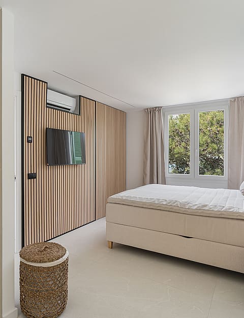 Contemporary bedroom featuring a vertical wood slat wall, upholstered bed, glass pendant lights, and garden views.