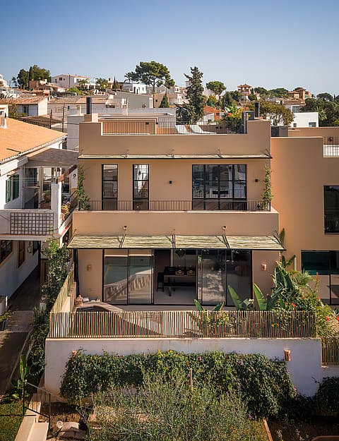 Exterior view of a multi-story townhouse in Genova with a sand-colored render, flat roof, and metal-framed windows.