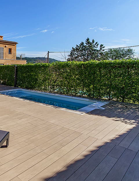 Exterior view of a Mediterranean stone townhouse with a rectangular swimming pool, sun loungers, and manicured hedge borders.