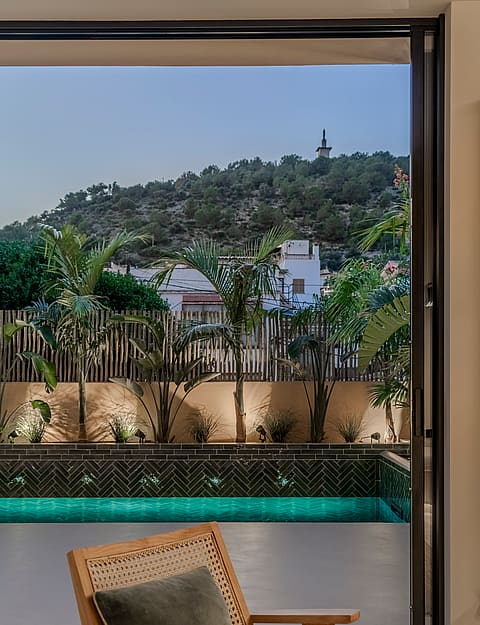 Contemporary wooden chair overlooking a dark-tiled pool and lush garden with a view of the Genova hills.