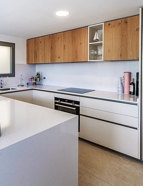 Modern U-shaped kitchen with white stone countertops, wood-veneer upper cabinets, and integrated appliances.