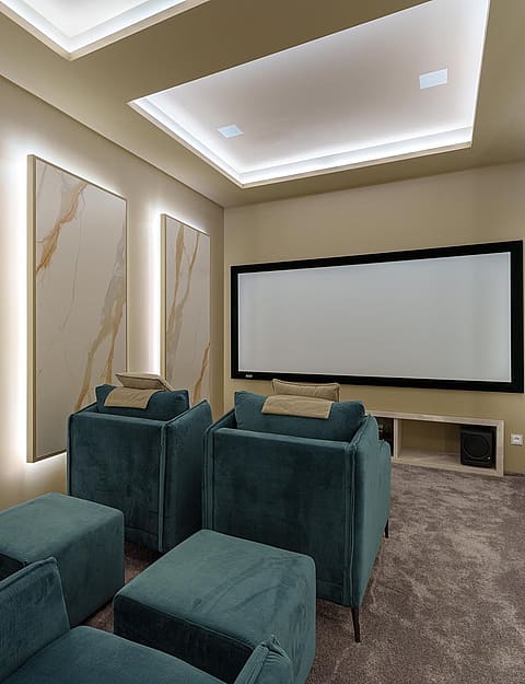 A private home cinema room with teal upholstered armchairs, large projection screen, and integrated LED lighting on walls.