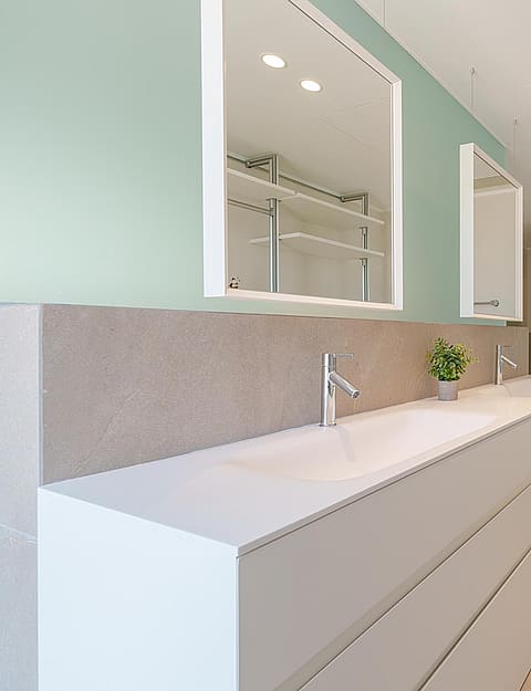 Baño moderno con doble lavabo blanco, pared verde salvia, dos espejos rectangulares y estanterías integradas.