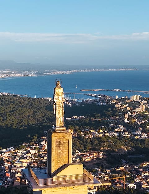 Aerial view overlooking the statue at Castell de Bellver with the city of Palma, harbor, and Mediterranean Sea in the distance.