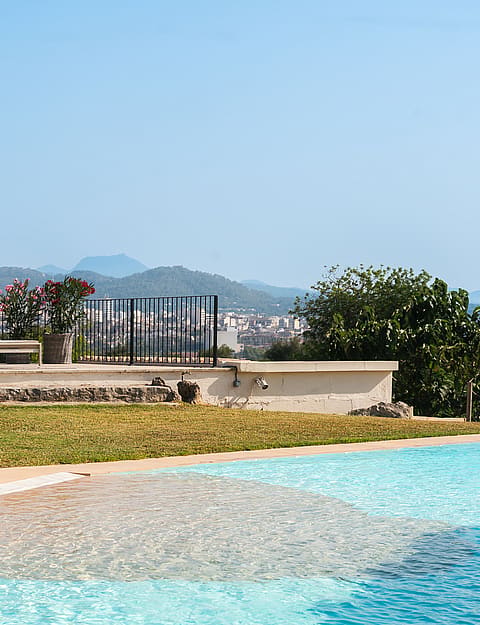 Piscina exterior en primer plano con terraza de piedra y tumbonas frente a las sierras a lo lejos.