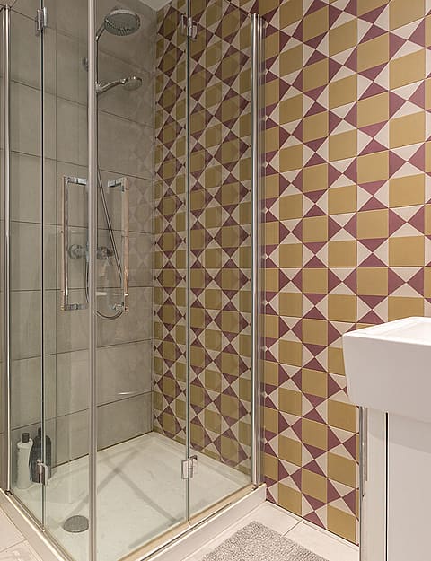 A compact modern bathroom featuring a walk-in glass shower, wall-mounted white toilet, and decorative geometric wall tiles.