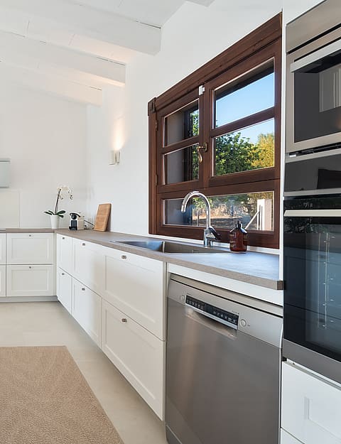 Cocina con muebles blancos, encimeras de piedra y marcos de madera bajo techos abovedados de madera blanca.