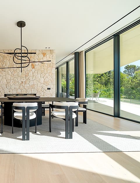 Dining area with dark rectangular table, six modern chairs, linear pendant light, and a prominent textured natural stone accent wall.