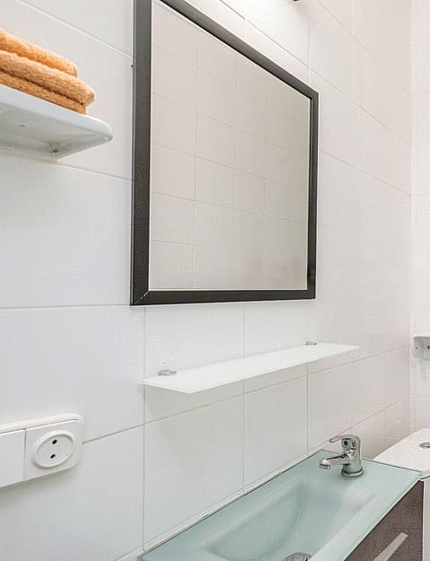 Modern bathroom with white tiled walls, a glass walk-in shower, a square mirror with a dark frame, and a glass vanity sink.