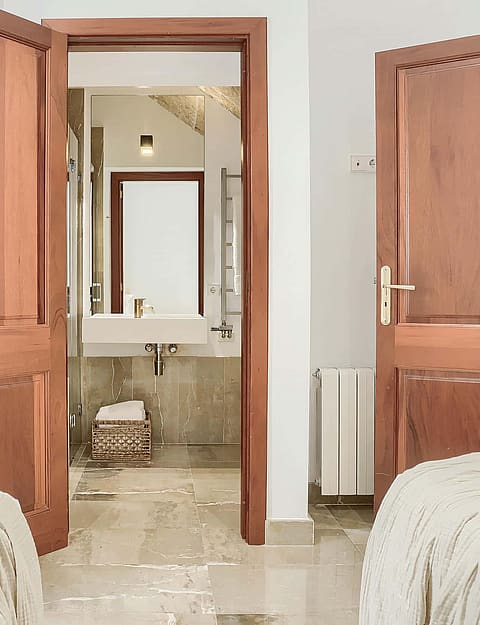 Interior view showing a bedroom leading into an en-suite bathroom through wooden double doors, featuring cream tile floors.