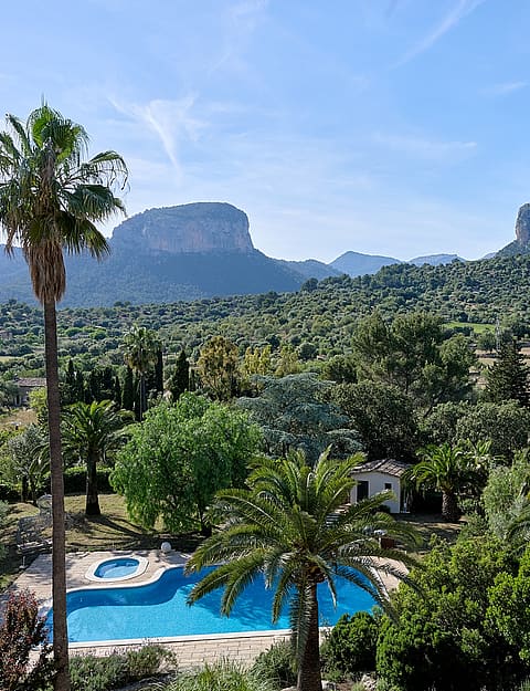 Wide shot of a Mallorca finca estate featuring a swimming pool, palm trees, and the Tramuntana mountain range in the distance.