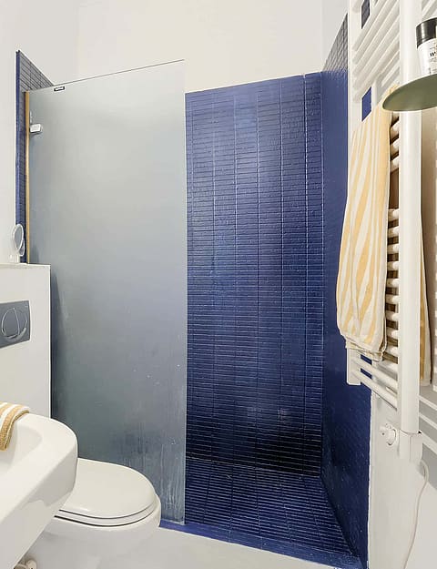 Interior view of a compact bathroom featuring a white sink, an oval wall mirror, and a walk-in shower with cobalt blue tiles.