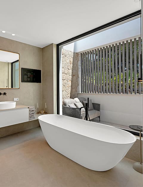 Spa-style bathroom with freestanding white bath, double vessel sinks, stone wall cladding and glazed opening to private terrace